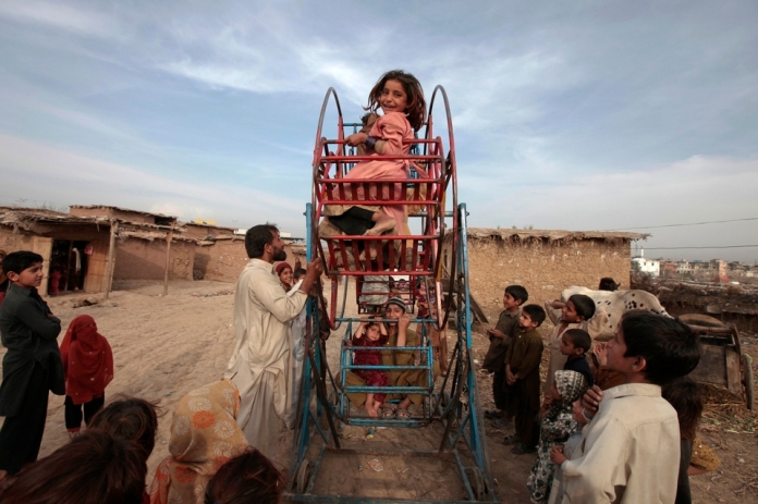 An Afghan girl smiles as she rides on a hand-operated ferris wheel with other children in a slum on the outskirts of Islamabad March 19, 2013. REUTERS/Faisal Mahmood (PAKISTAN - Tags: SOCIETY)